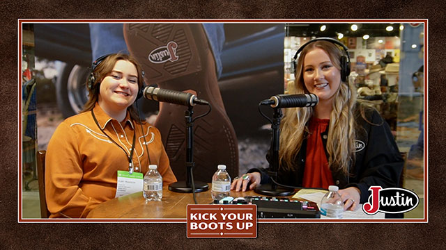 Two women talking to each other, sitting down, smiling at the camera.